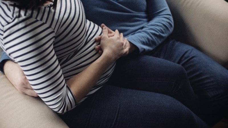 The lower halves of a man and a pregnant women sit together and place their hands on the woman's belly.